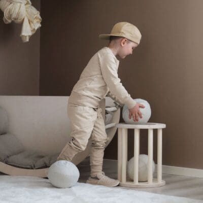 Lapsi laskee HILLA pallon LUOTO jakkaran sisään sen ollessa korina. Takana näkyy myös LUOTO kiipeilykaari ja KAURA pehmuste.